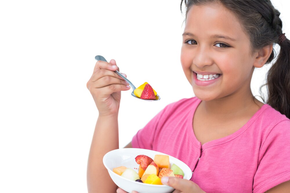 Smiling girl eating a bowl of fruit salad.