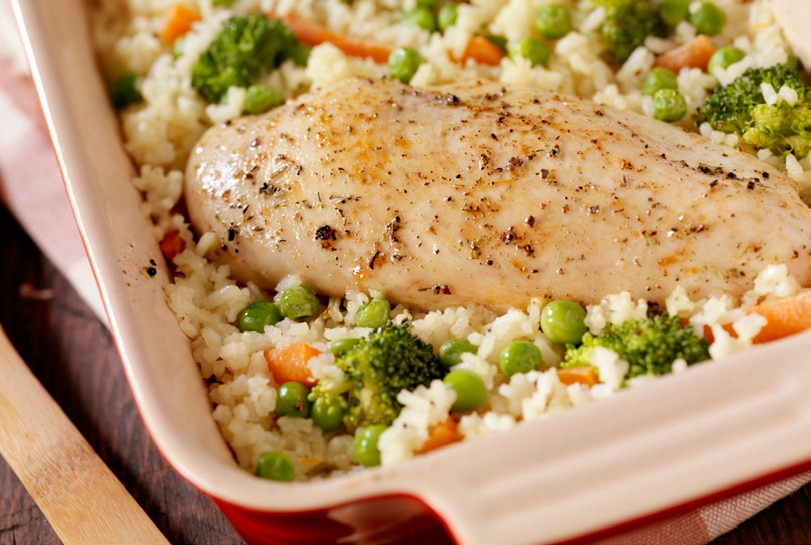 Baking dish with roasted chicken, peas, carrots, and rice.