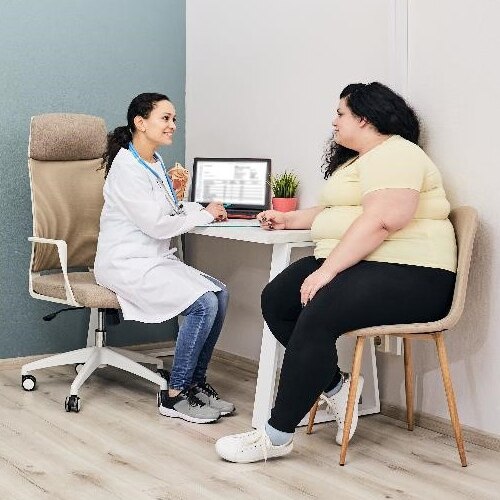 A health care professional talks in her office with a young woman who has obesity.