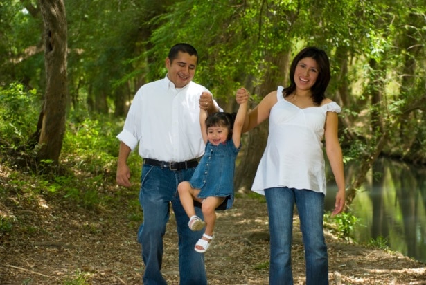 A pregnant woman walks in the woods with her husband and young daughter.
