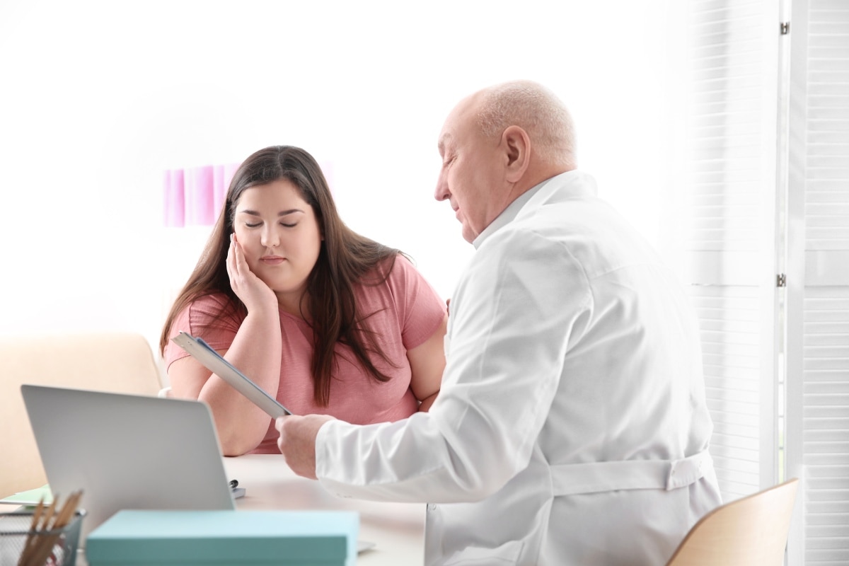 A health care professional talks in his office with a woman who has obesity.