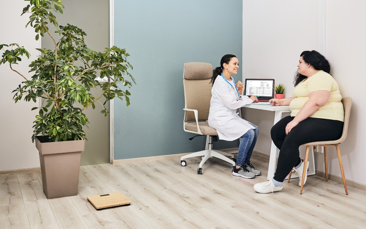 A health care professional talks in her office with a young woman who has obesity.