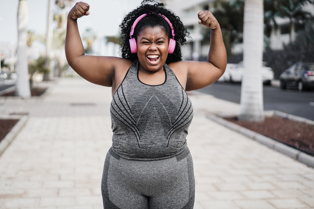 Smiling woman in workout clothing lifts her arms in celebration.