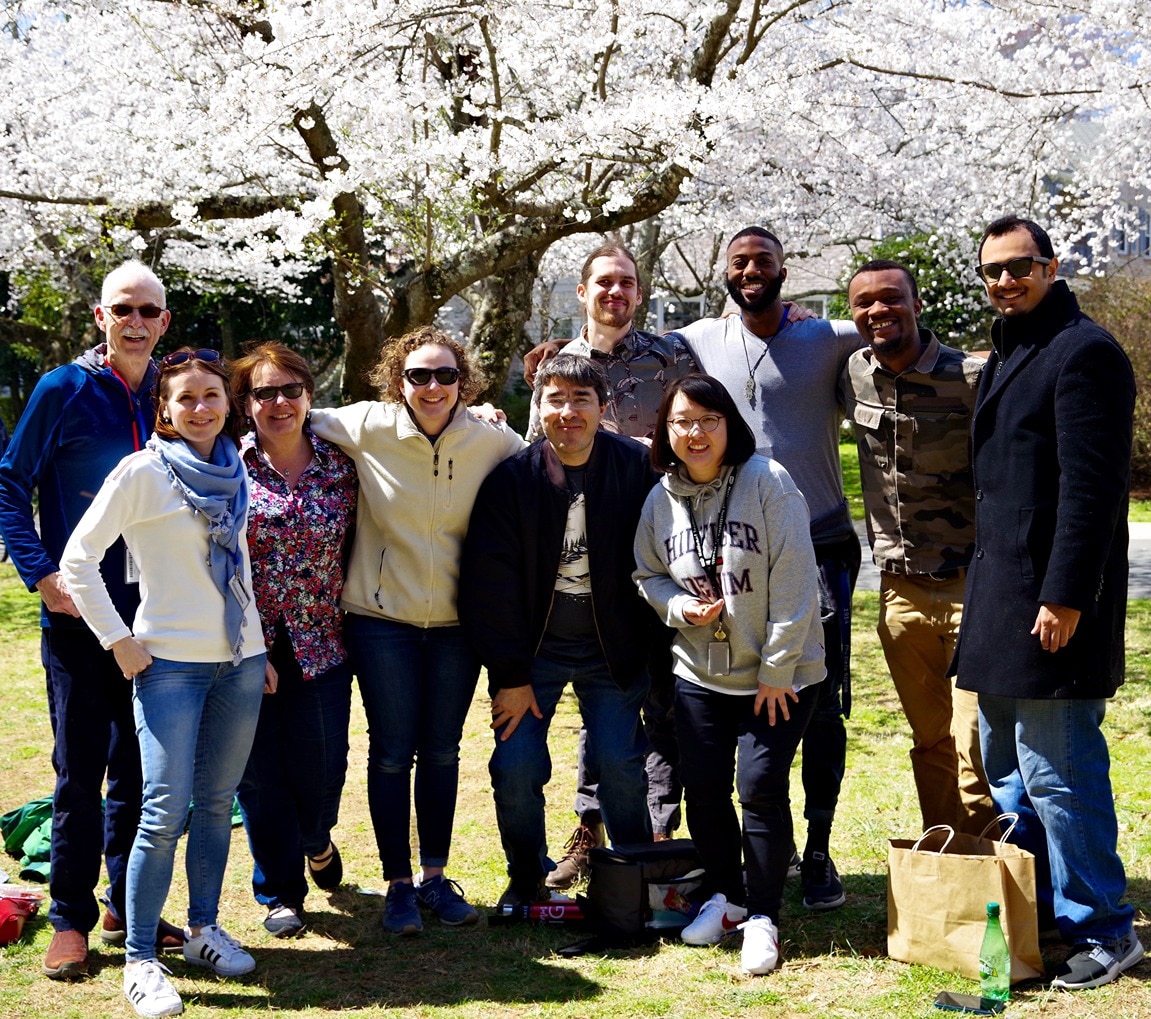 Group of people in winter clothing standing in front of a blooming cherry blossom tree.