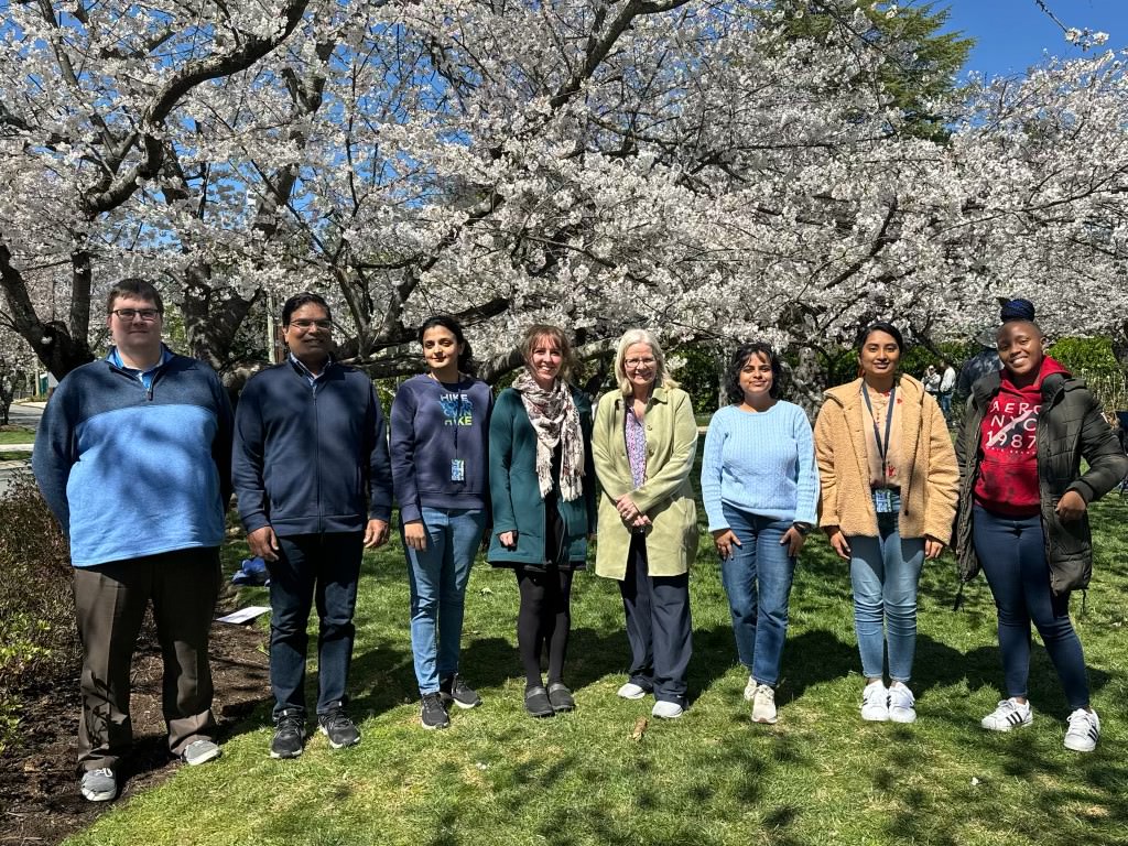 NIDDK Structural Cell Biology Section lab members stand and smile in front of cherry blossoms trees.