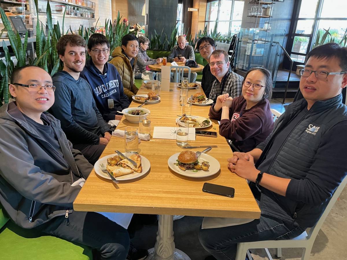 Lab members sitting at a rectangular table with food in front of them.