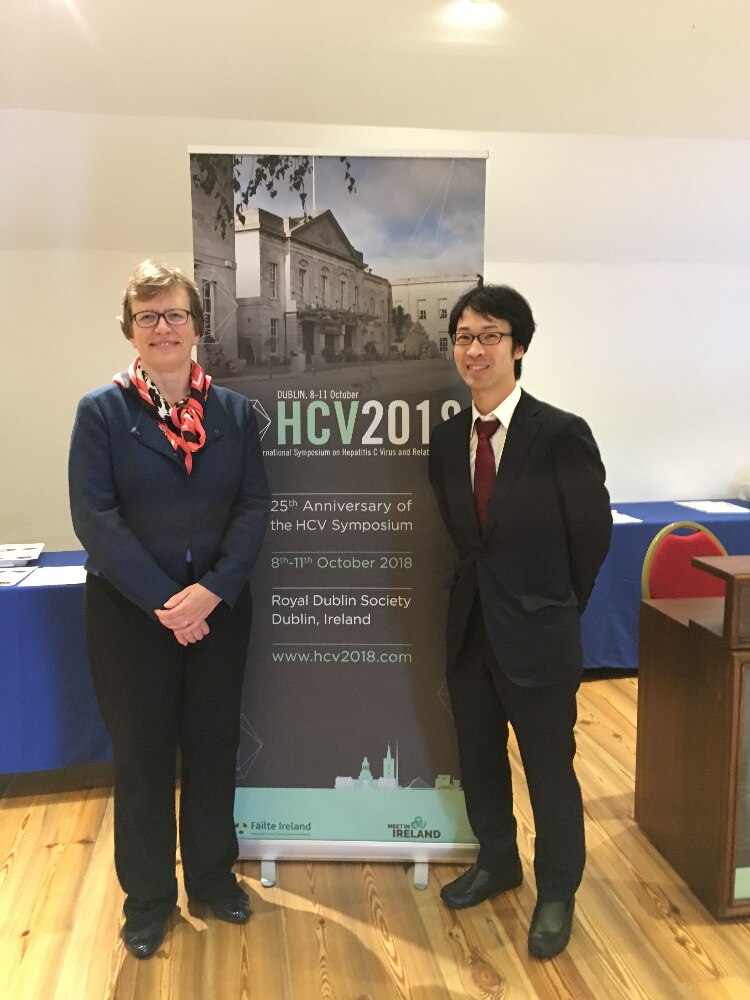 Two lab members pose in front of an HCV 2018 banner